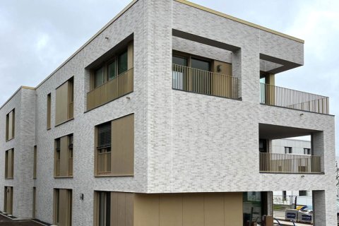 Gebäudeausschnitt einer Fassade mit hellen Steinen und beigefarbenen Blechverkleidungen, großen Fensterflächen und Loggien