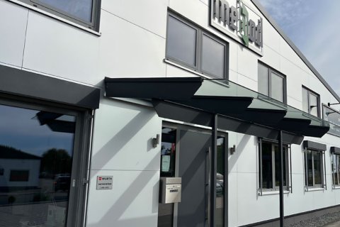 Eingangsfassade mebod Ausschnitt Fassade Eingangsbereich mit Glasvordach und Metallkonstruktion sowie weißer Metallfassade