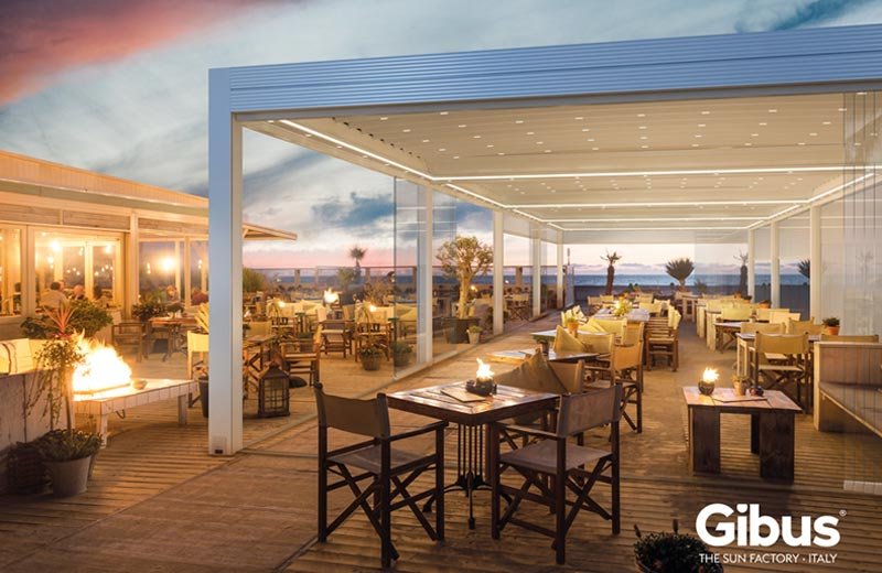 Vue sur une pergola (de Gibus) d'un restaurant avec des éléments vitrés coulissants au coucher du soleil